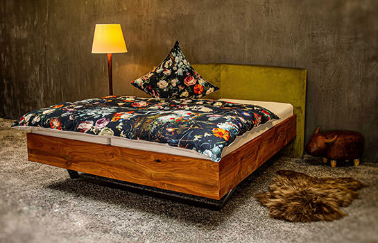 Massivholz-Bett Grünli, seitliche Ansicht. Rahmen aus Kirschenholz, auf einer polierten Edelstahlkufe, Kopfteil grüner Samt-ählicher Stoff. bodentief.