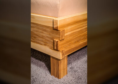 Massivholz-Bett Eschenputtel, Nahaufnahme der Verzahnung zwischen Seitenrahmen und Fußteil. Kanten gefast. Rahmen auf Blockfüßen.
