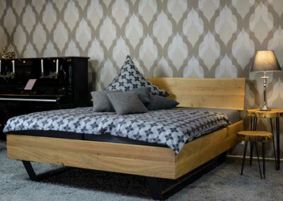 Massivholz-Bett Hörmen, seitlich Das massive Eichenbett besticht durch seine moderne, aber schlichte Optik. Das Bett ist geschliffen, lackiert und steht auf Stahlkufen, das Kopfteil ist einteilig mit Baumkante.
